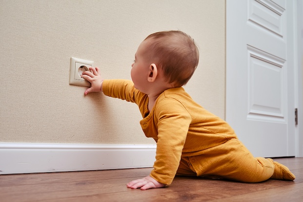 A baby crawling and touching an outlet cover.